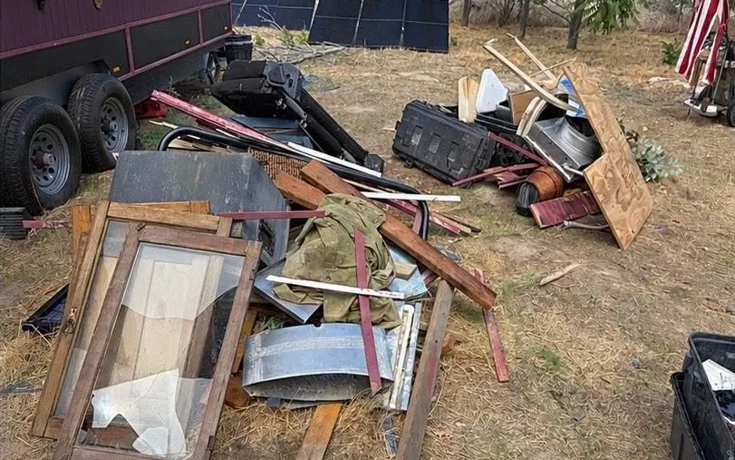 Before: old windows, lumber and scrap metal piled on dry ground beside a trailer