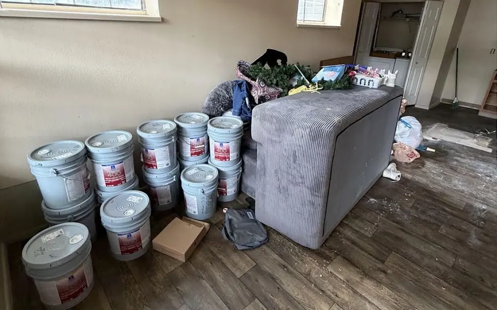 Before: a spare room with a grey couch, bags, boxes and a row of buckets on the floor