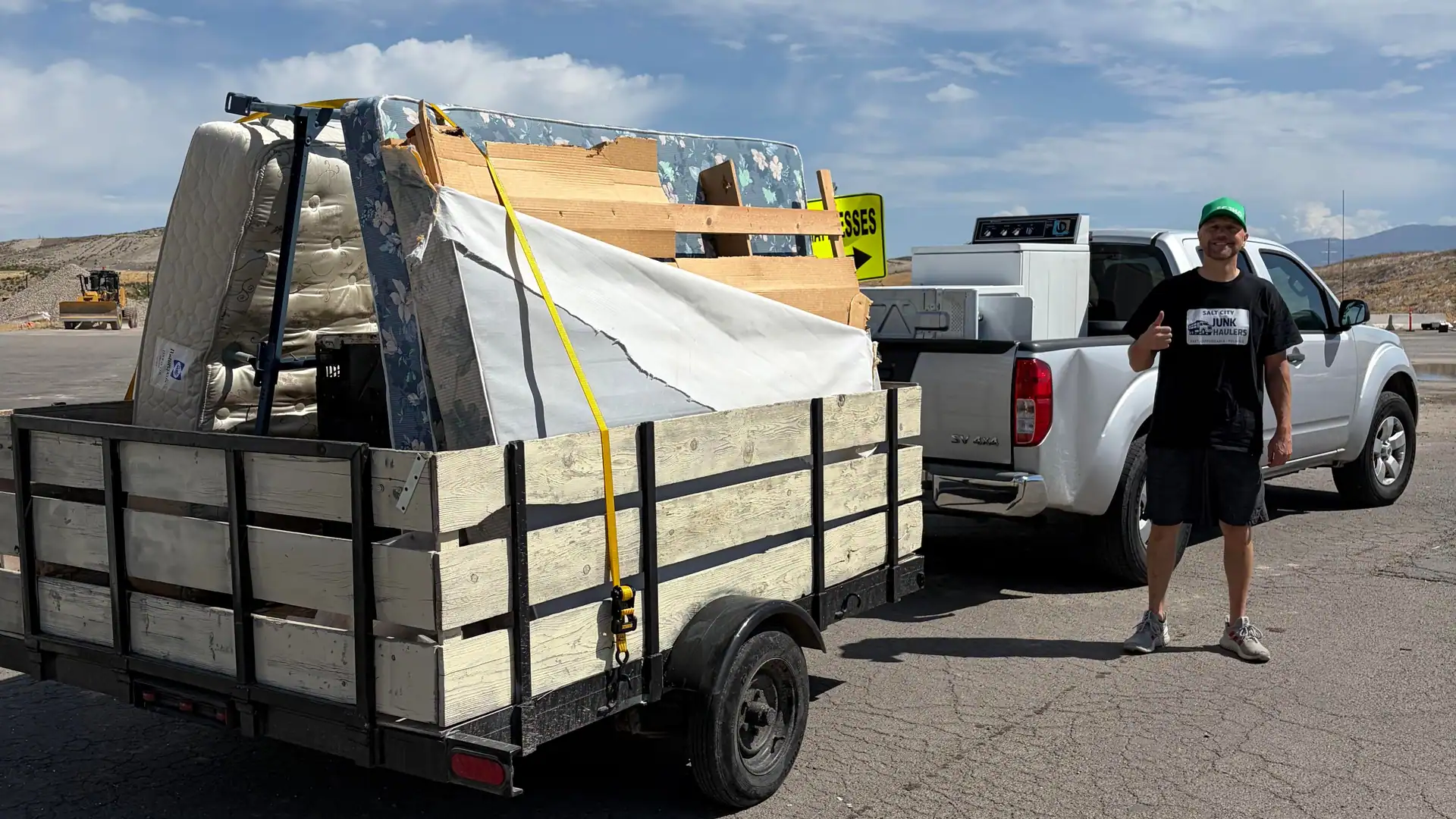 Trailer stacked with mattresses, box springs and lumber, with a washer in the truck bed, at the transfer station