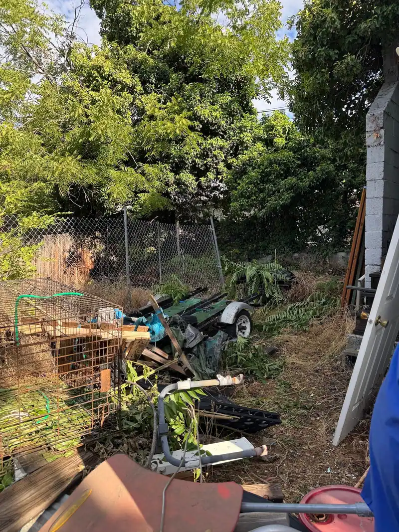 Backyard piled with old cages, scrap metal, and yard debris before a cleanout