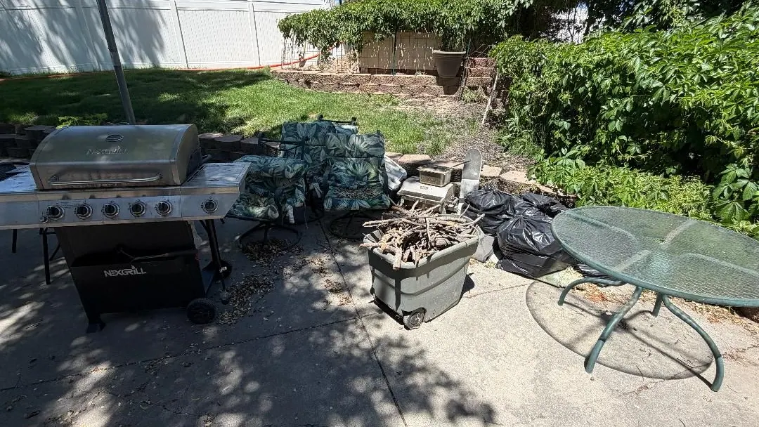 Backyard patio with an old grill, patio furniture, and bagged junk waiting for pickup