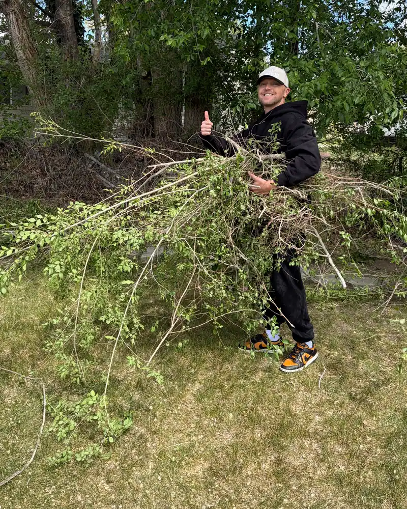 Jeremy carrying an armful of tree branches on a yard cleanup, thumbs up
